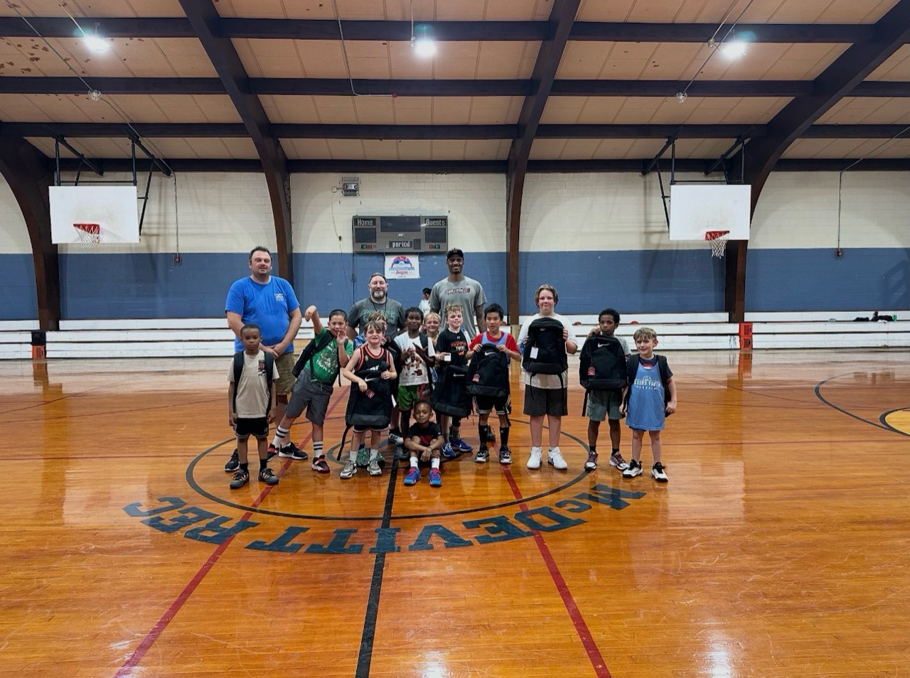 McDevitt Rec Basketball players and coaches pose together at center court in a gym.